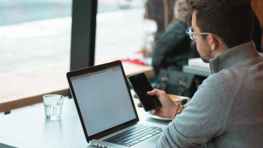 Man holding phone while sitting in front of a laptop