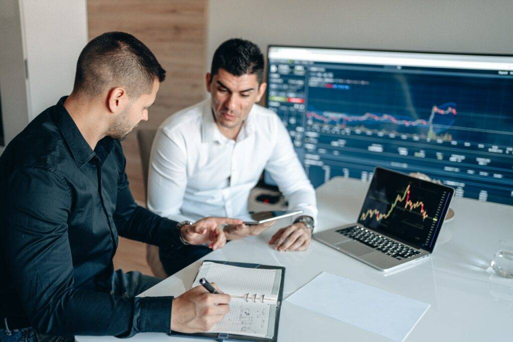 Two people discussing graphs on tablets and laptops