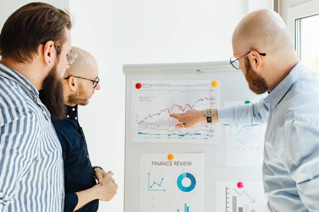 Three people pointing at graphs pinned to a board