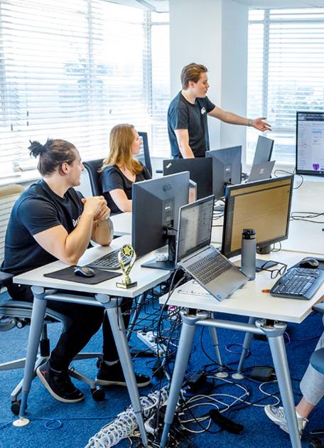 Three people discussing using computers on a desk