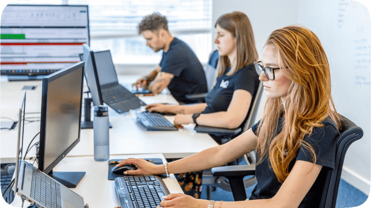 Three people working on computers at a desk