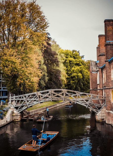 A river with people on small boats, and a wooden bridge crossing over the top