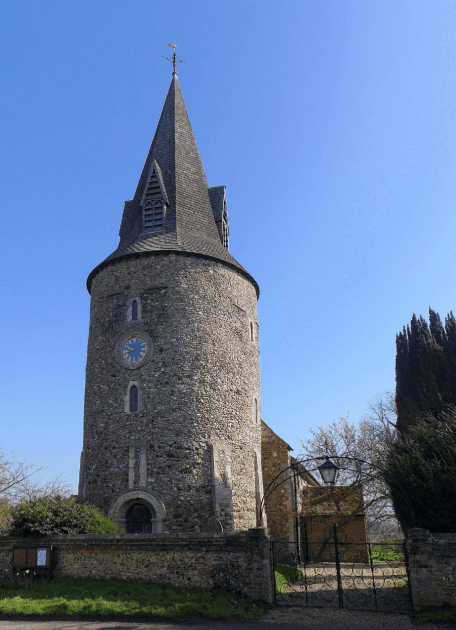 A tall cylinder building behind a gate with a clock face on the building